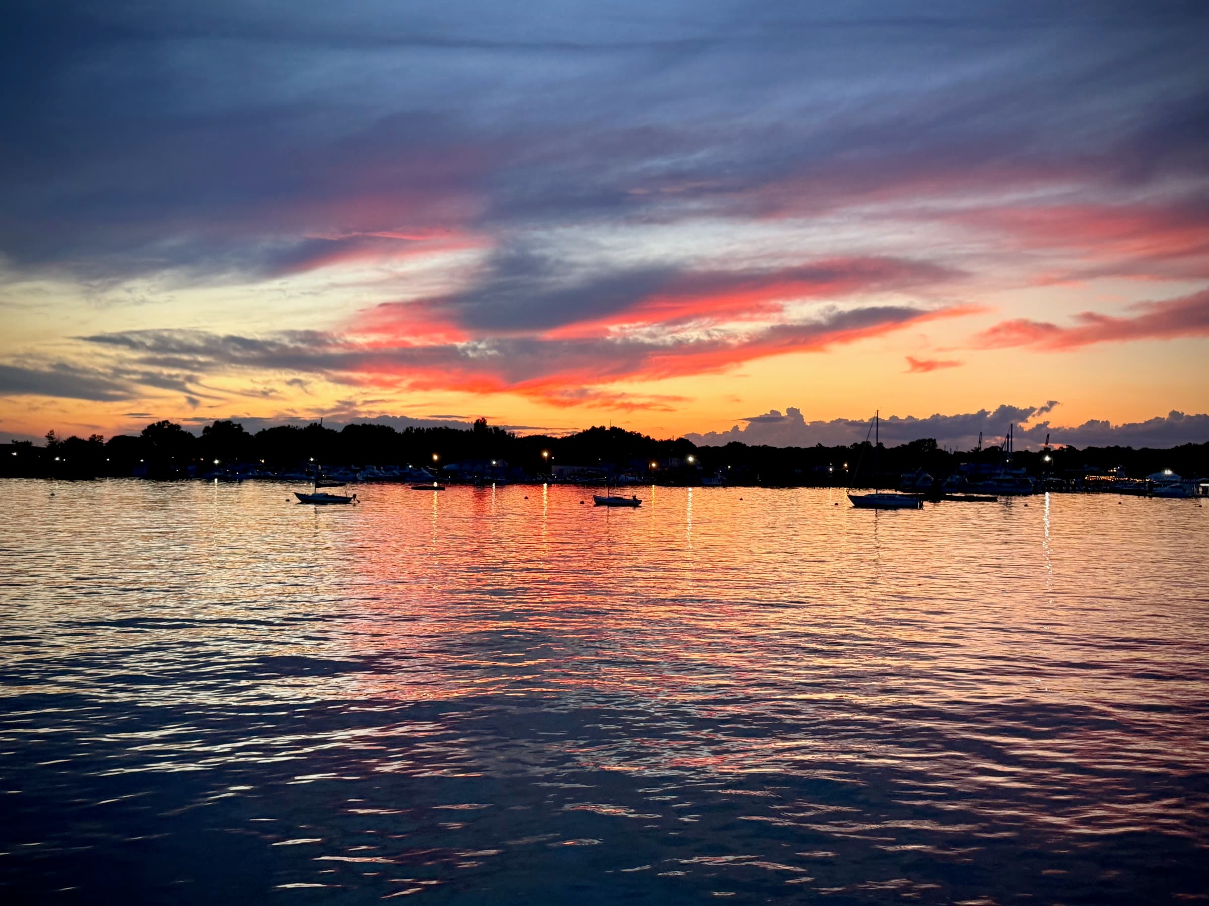 Boats resting on Manhasset Bay beneath a vivid sunset photographed from Town Dock.