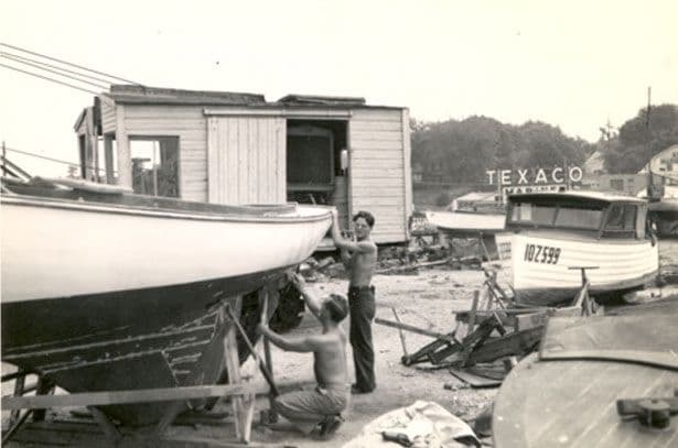 Two shirtless boatyard workers repairing the hull of a sloop at A and R Marshall in 1943