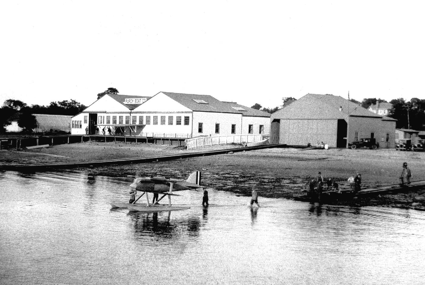 The Purdy Boat Company shop viewed from Manhasset Bay with a racing seaplane floating in front